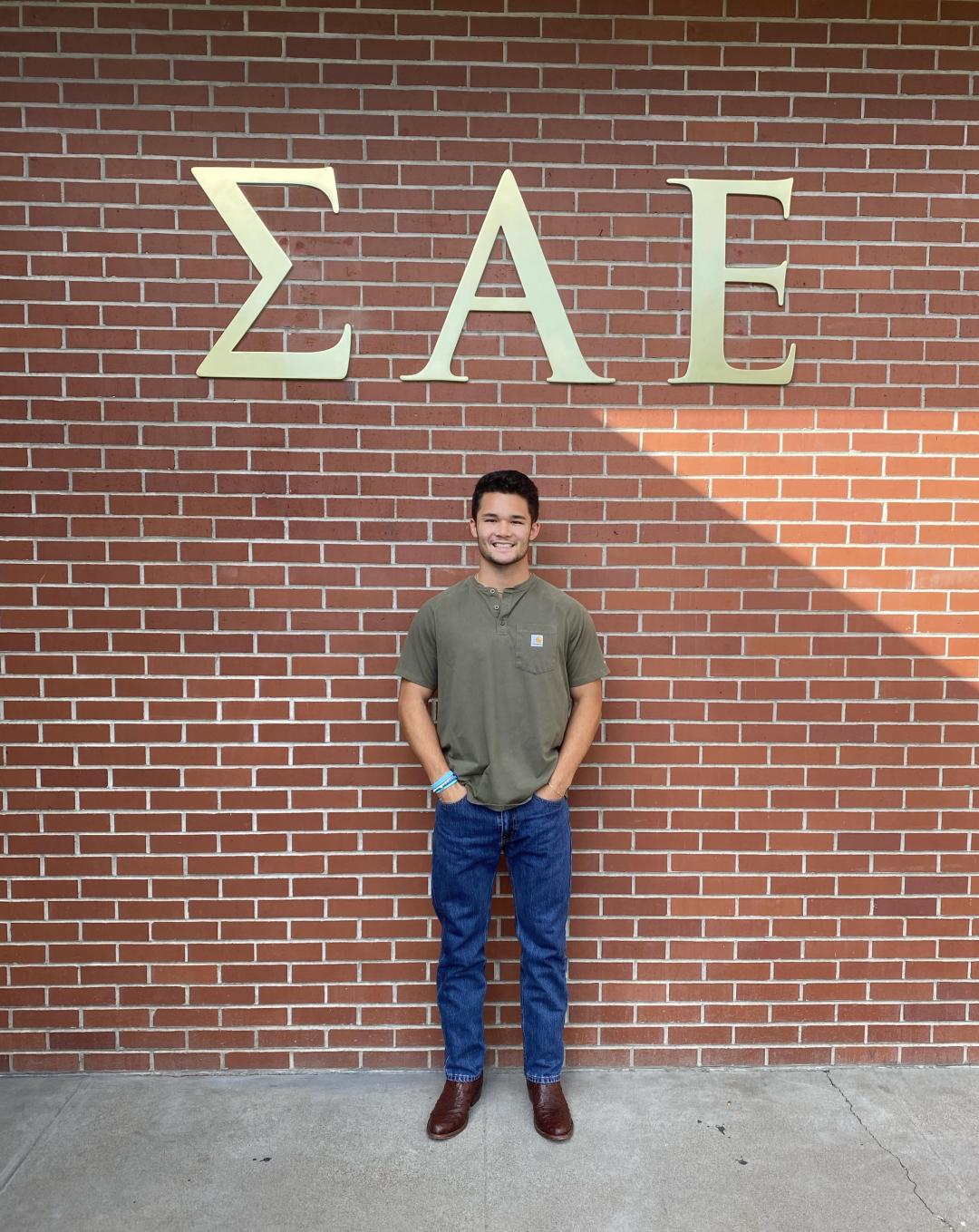 Young man standing in front of a wall with fraternity letters Sigma Alpha Epsilon
