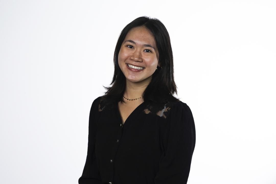 A woman in a black shirt poses for a headshot in front of a white background.