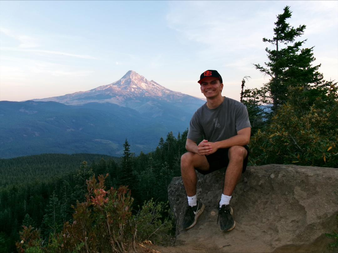 A man poses for a photo with a mountain in the background.