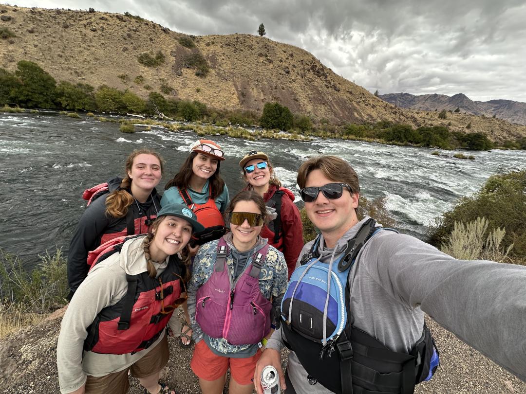 A group of people wearing life jackets pose for a photo while on a river rafting adventure.