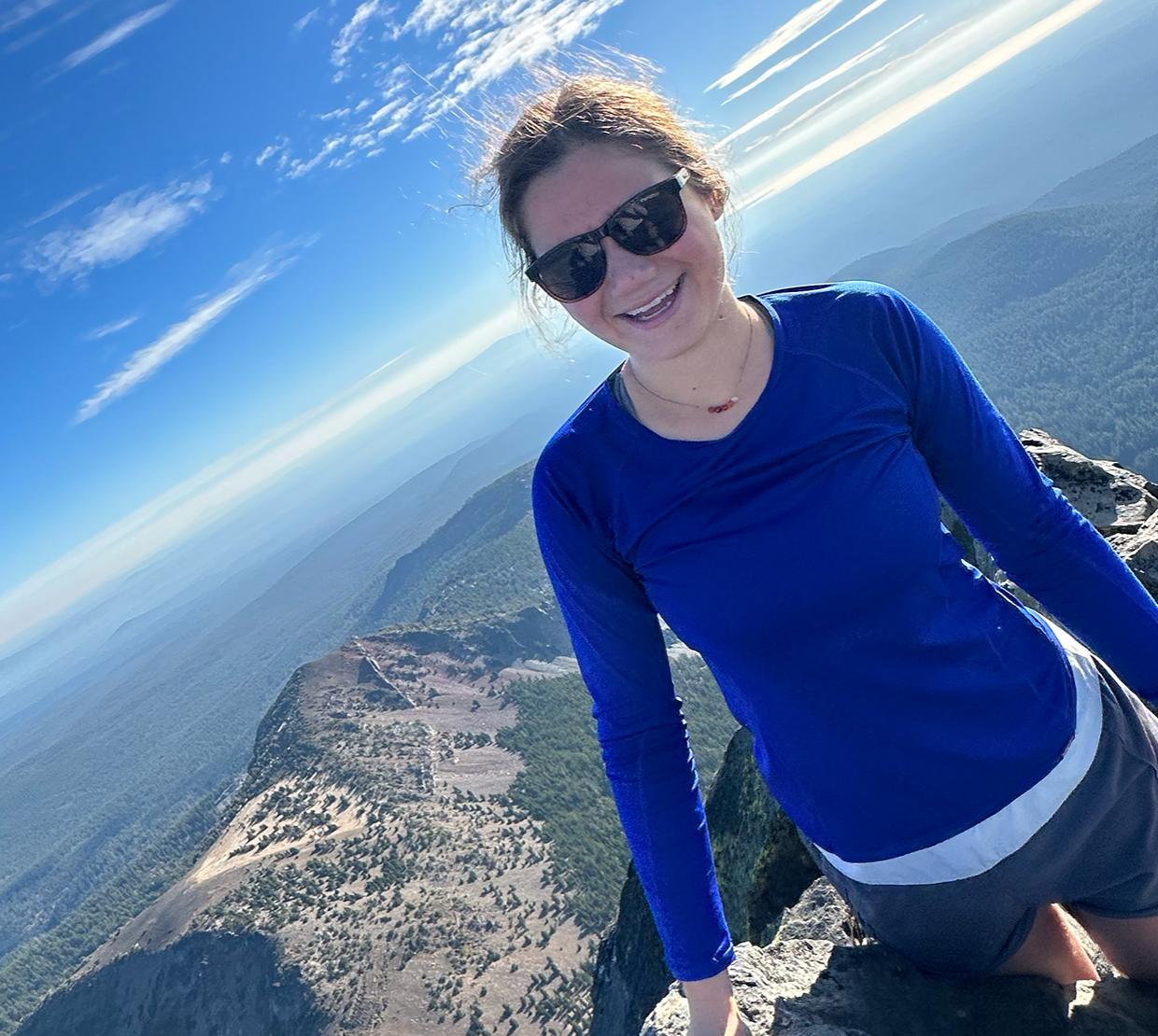 A woman in a blue shirt on top of a mountain.