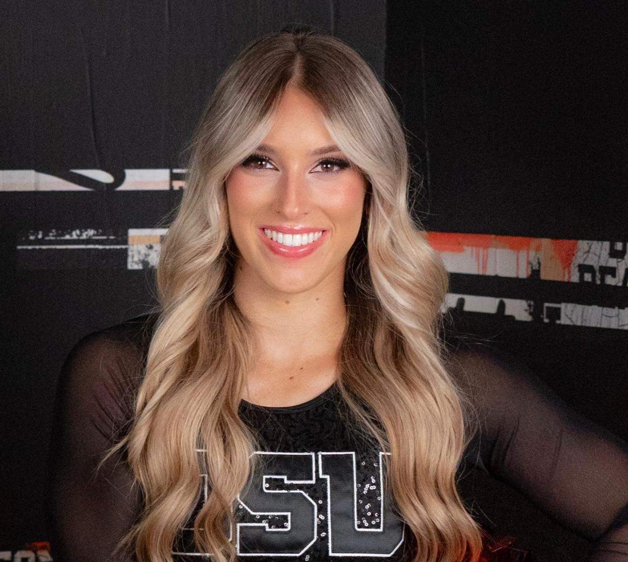 A headshot of a woman with wavy blonde hair smiling at the camera wearing a black OSU cheer uniform. 