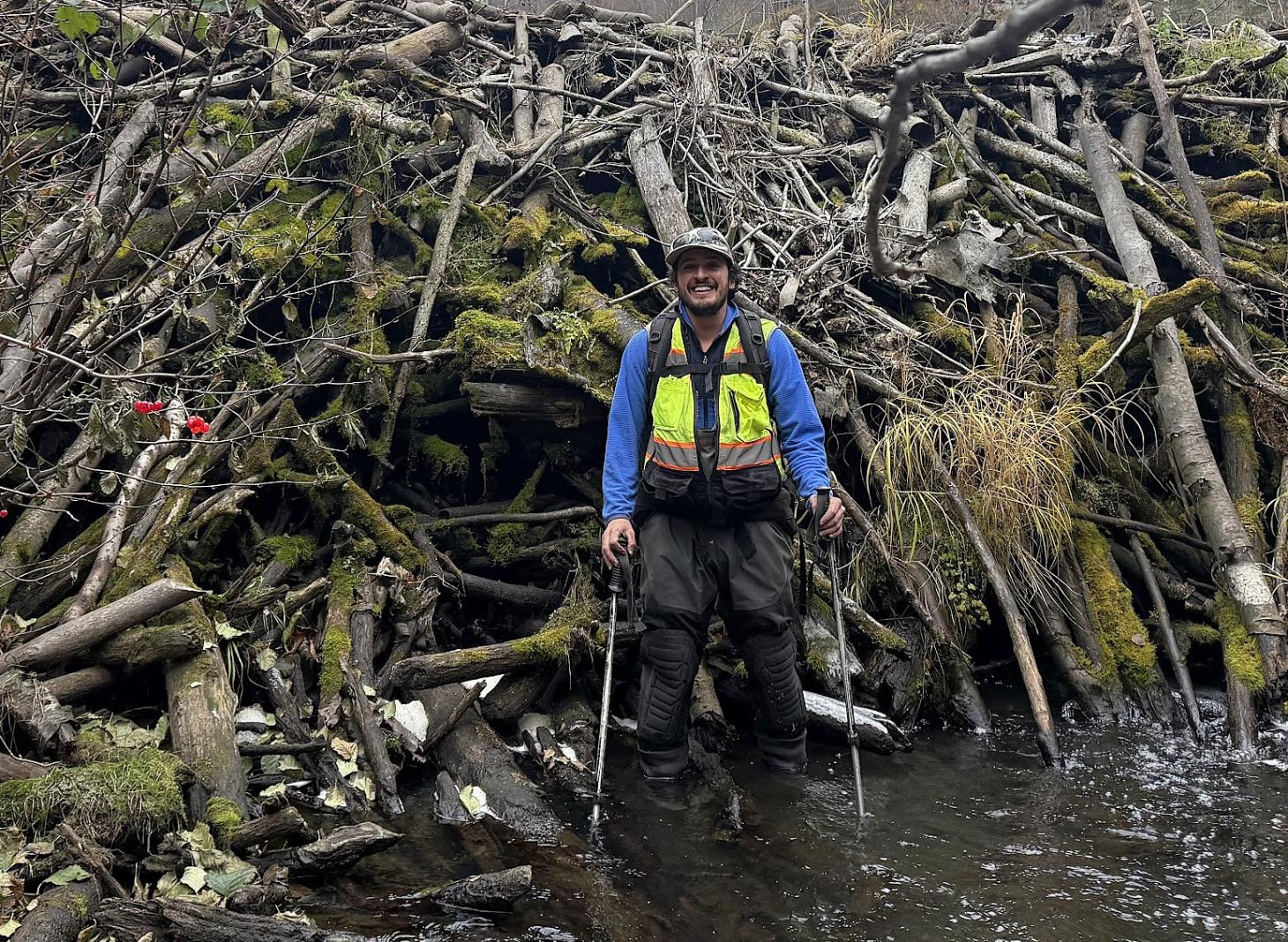 Ben Americus standing in front of a beaver dam that is almost twice his height.