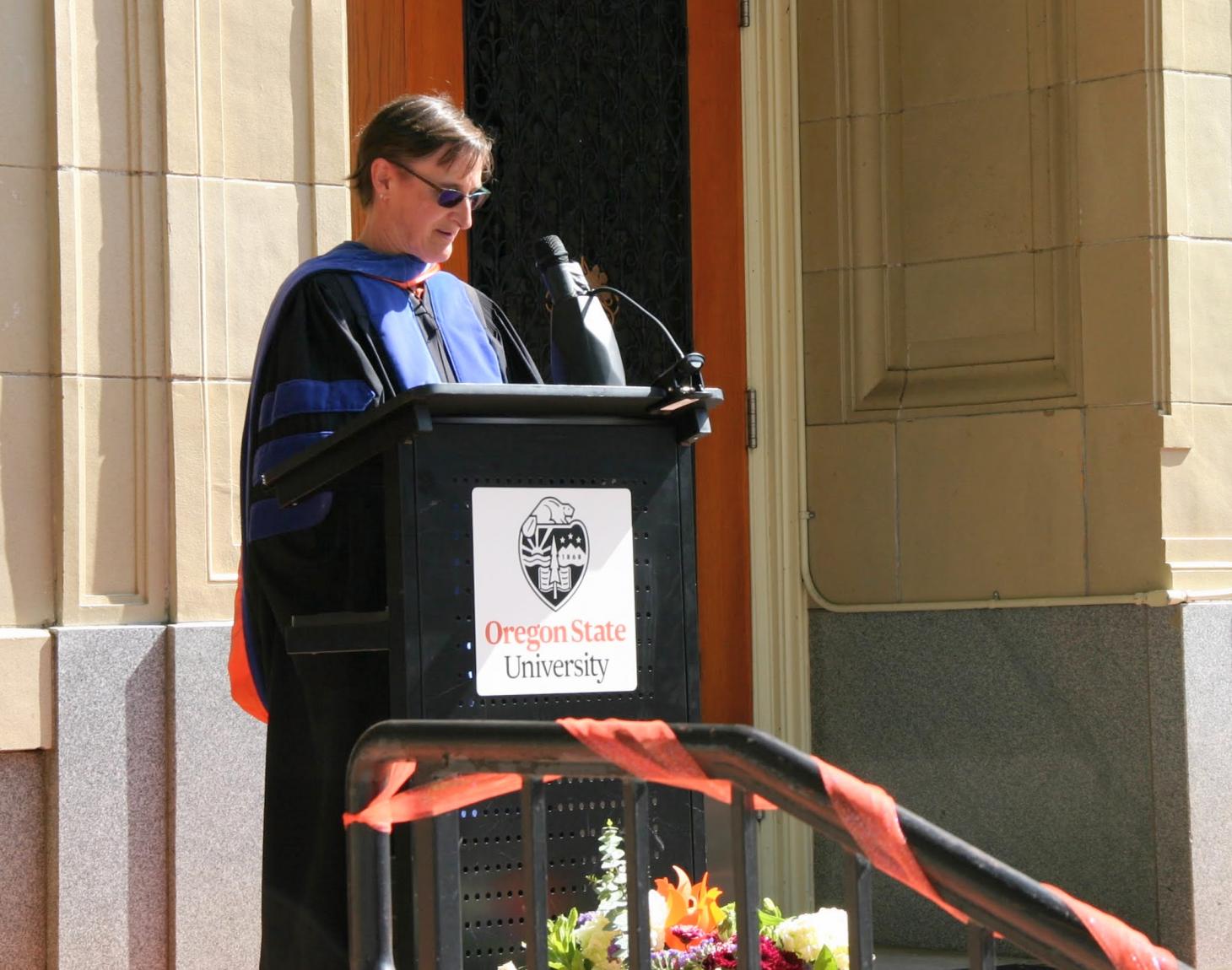 Dr. Linda Bruslind reads student names at a podium in front of Kidder Hall.