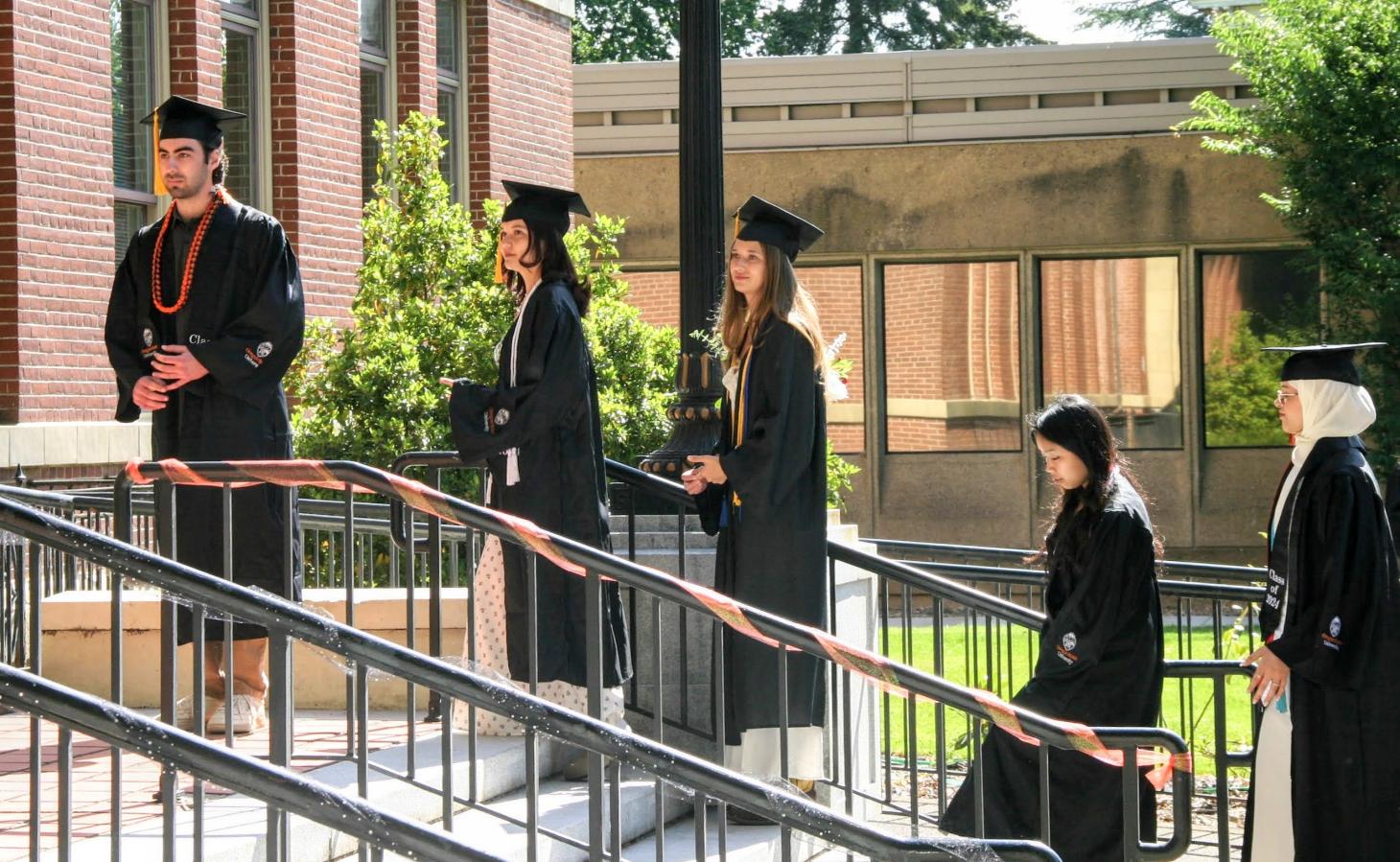 Students in graduation caps and gowns line up in front of Kidder Hall.