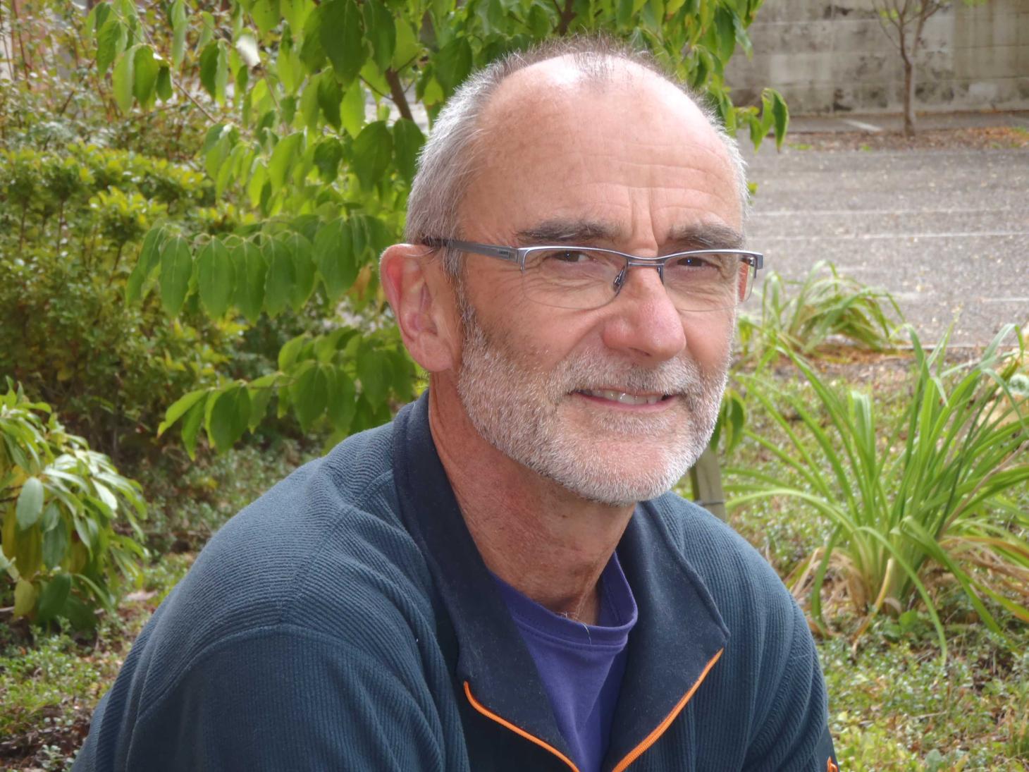 Peter Bottomley sits outside with plants in the background.