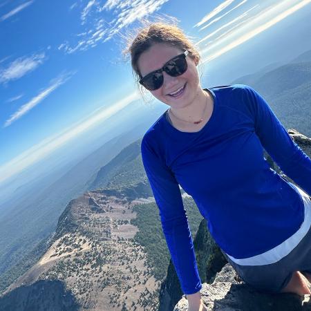 A woman in a blue shirt on top of a mountain.