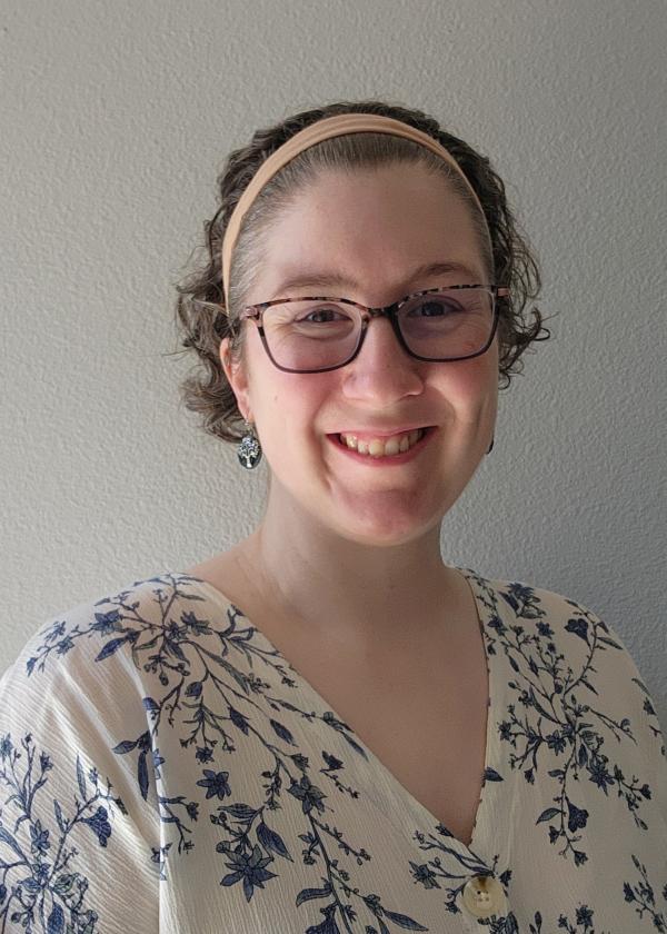 Portrait of Alice Naftaly standing against a white wall.