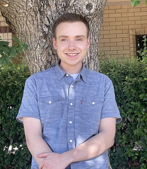 Photo of Nicholas Bellavia in a blue shirt standing in front of a tree.