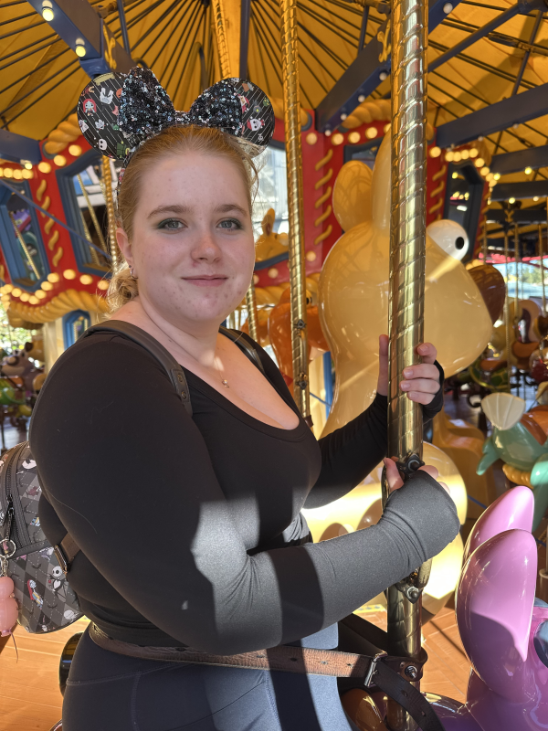Photo of Paige Clark riding a carousel and wearing Mickey Mouse ears.