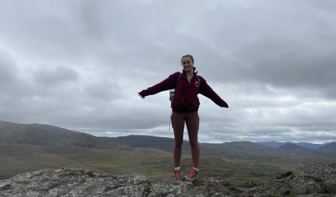 Amelia Noall standing at the top of Torc Mountain in Ireland, overlooking a vast field.