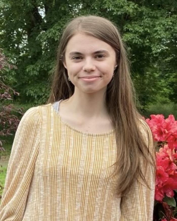 Photo of Tara Conrad in a yellow sweater in front of blooming flowers.