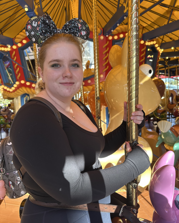 Photo of Paige Clark riding a carousel and wearing Mickey Mouse ears.
