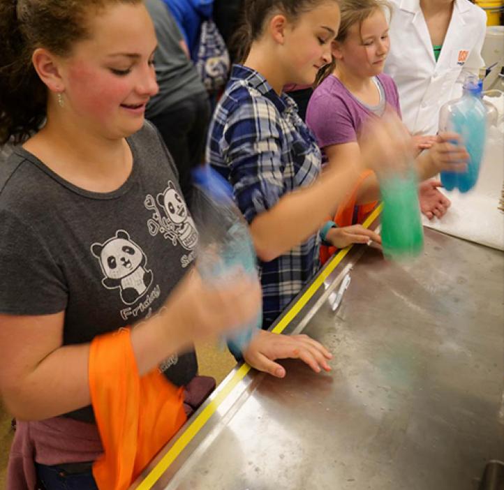 Middle school students shaking colored bottles in lab.