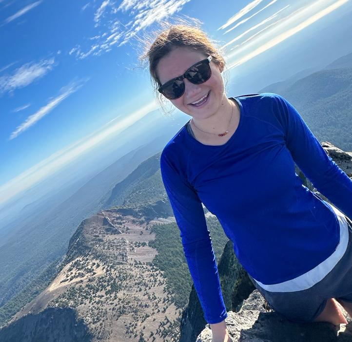 A woman in a blue shirt on top of a mountain.