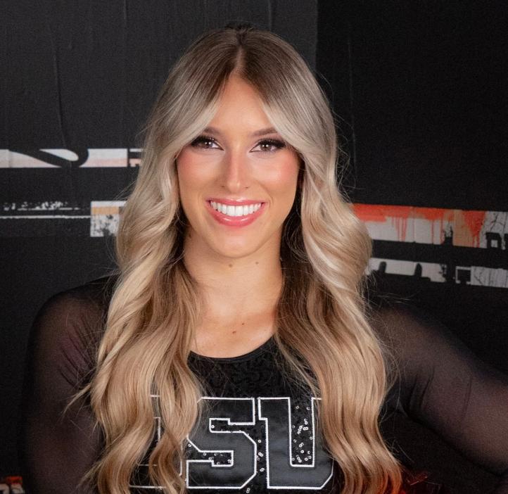 A headshot of a woman with wavy blonde hair smiling at the camera wearing a black OSU cheer uniform. 